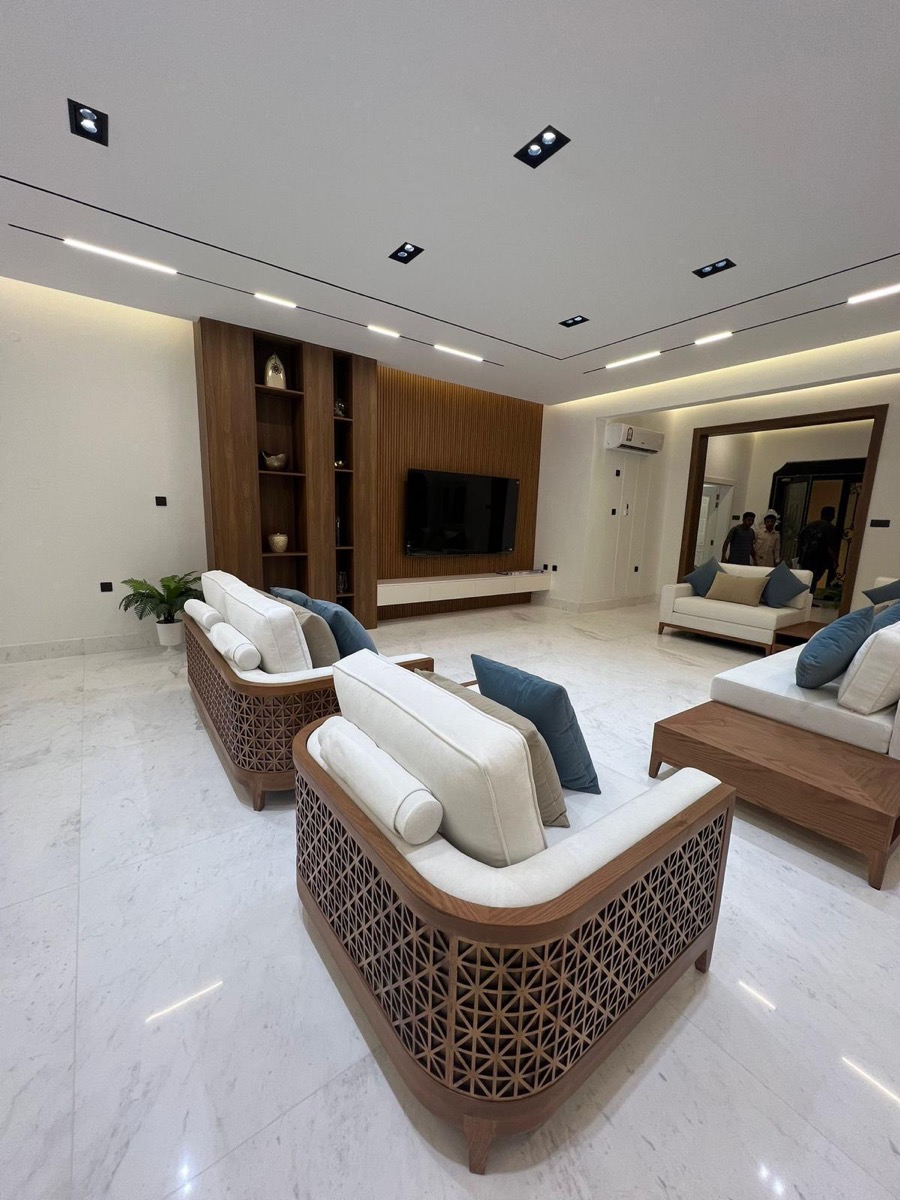 Before: A majlis, before and after. The raw shot has workers in the mirror and an AC unit on the wall. The final image is the same room, staged and lit like a showroom.